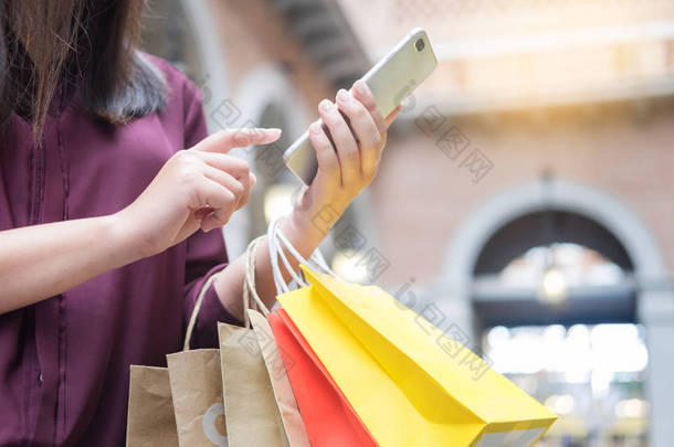 在享受一天购物的同时, 女人在商场里看着带纸袋的手机