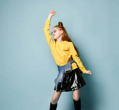 活跃的红头发少女，穿着黄色运动衫和光滑的黑色裙子，手举着手跳舞，感觉很惬意