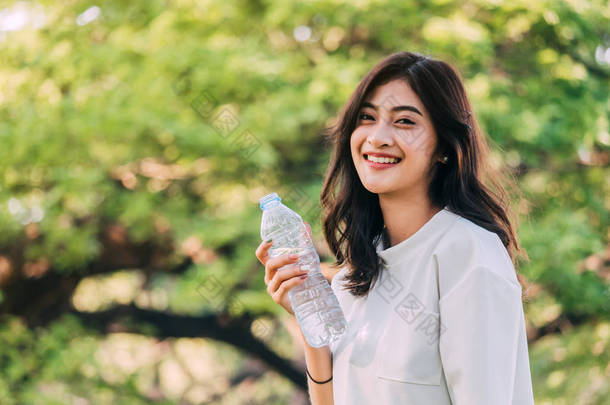 美丽的女人在夏日的绿色公园喝水。<strong>健康</strong>的生活方式概念