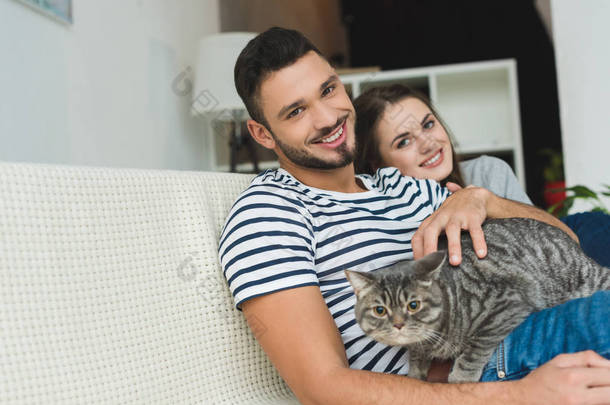 美丽的年轻夫妇与可爱的<strong>小花猫</strong>坐在沙发上