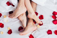 部分看法赤脚夫妇躺在柔软的白色床上用品与红色花瓣 