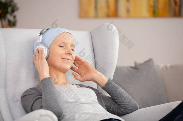 癌症治疗后, 带着耳机和蓝色头巾在家休息的宁静妇女