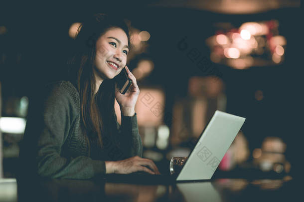 漂亮迷人的亚洲女人，带着笔记本电脑微笑工作，用智能手机与顾客交谈，以获得在咖啡店、商业概念、暖通等办公室外工作的成功理念和要求