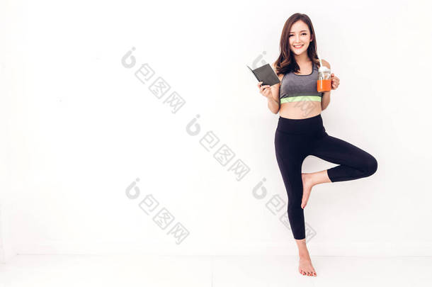运动妇女在运动衣放松阅读一本书和喝新鲜<strong>果汁</strong>后锻炼反对复制空间添加文本与白色墙壁<strong>背景</strong>。饮食概念。健身和健康的生活方式