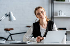 微笑的女商人在正式穿坐在电脑桌在工作场所