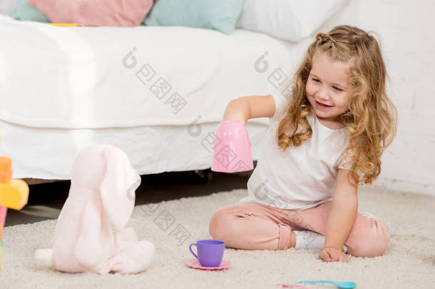 可爱的快乐的孩子玩兔子玩具和塑料杯在儿童房