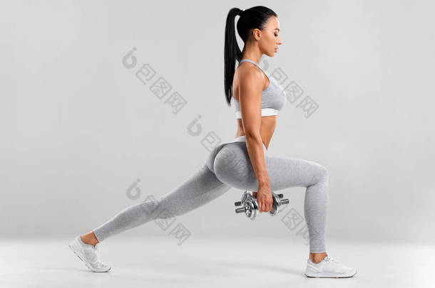 健美的女人为了进行腿部肌肉锻炼而做隆起运动。在灰蒙蒙的背景下，活跃的女孩向前迈了一步