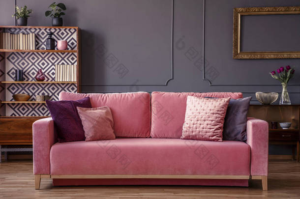 粉红色天鹅绒沙发与装饰枕头站在灰色客厅内部与<strong>老式</strong>橱柜, 新鲜的植物和墙上的造型
