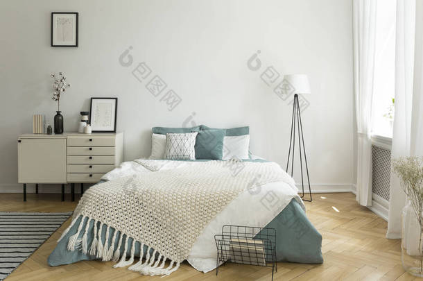 一张舒适的大床, 里面有苍白的绿白色亚麻布, 枕头和毯子, 在一个女人明亮的卧室里有窗户。真实照片.