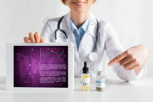 幸福的医生拿着带医疗应用的数码平板电脑，用手指指尖瓶口，刻有cbd字母的照片 