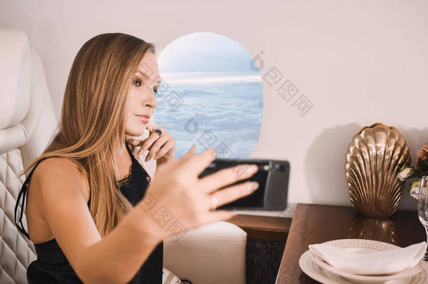 美丽的年轻女孩在商务舱的商务舱与手机在她的手中舒适豪华旅行