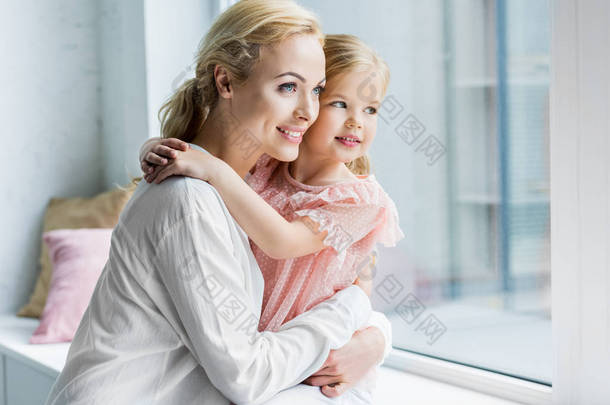 美丽幸福的母亲和女儿拥抱和看窗口
