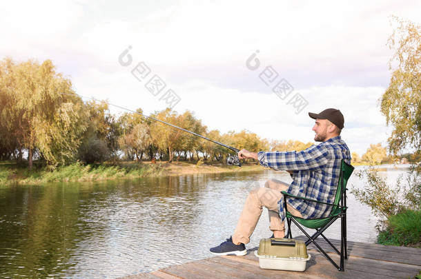 男子与鱼竿钓鱼在木码头在河边。娱乐活动