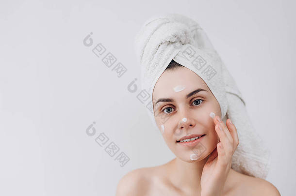 皮肤护理。一个美丽和微笑的女人使用护肤品, 润肤霜或化妆水照顾她的干<strong>肤色</strong>。把润肤霜涂在她脸上。文本的位置