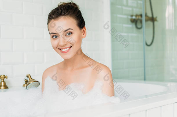 美丽的快乐的年轻女子在相机<strong>微笑</strong>, 而放松在浴缸与泡沫