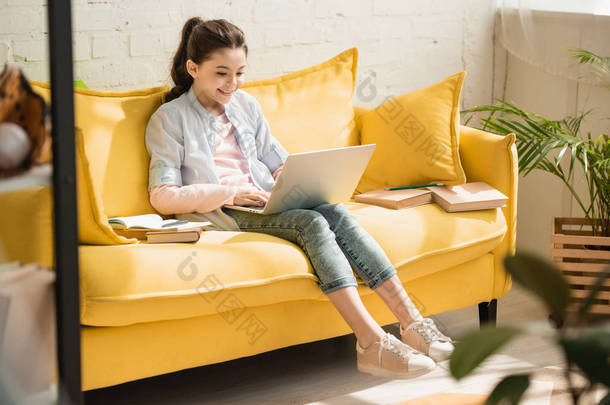 可<strong>爱</strong>的孩子使用笔记本电脑，而坐在黄色的SONS，靠近书籍在家里