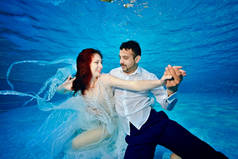 一对相爱的夫妇，一个女孩和一个混血儿在阳光明媚的日子，穿着婚纱在室外游泳池里游泳和在水下玩耍。不寻常的婚礼.