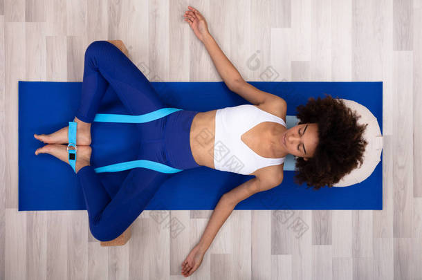 放松的年轻女子躺在<strong>健身</strong>垫做运动与瑜伽带和两个块