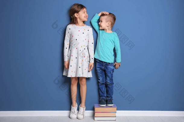 小女孩和男孩测量他们的高度在颜色墙壁附近