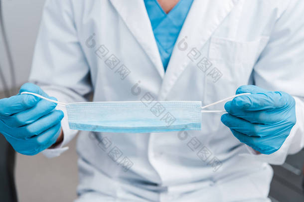 穿着蓝色乳胶手套的男子拿着医疗面具的裁剪视图 