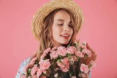 关闭了一个美丽的年轻女子在夏季礼服和草帽持有康乃馨花束隔离粉红色背景的肖像