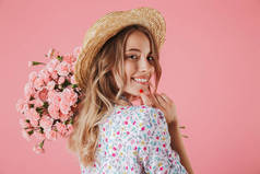 关闭一个美丽的年轻女子在夏季礼服和草帽捧着康乃馨花束, 看着她的肩膀被孤立的粉红色背景的肖像