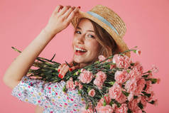 关闭一个可爱的年轻女子在夏季礼服和草帽持有康乃馨花束隔离粉红色背景的肖像