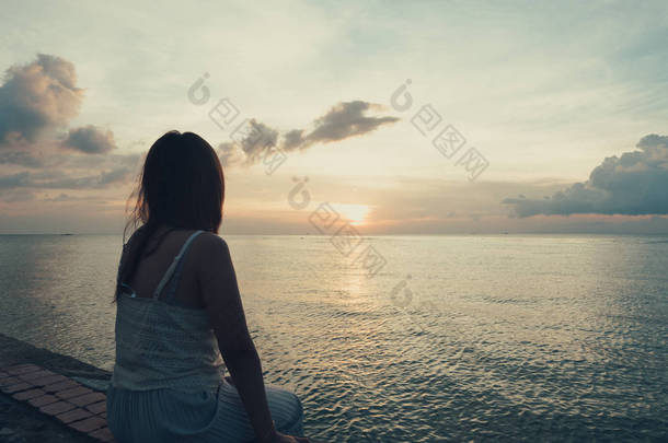 年轻女子的剪影独自坐在后侧户外在热带岛屿海滩失踪的男朋友和家人在夏天的日落。悲伤和孤独的概念在黑暗和复古色调.