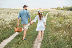 带野餐篮的情侣在野外散步时的后视