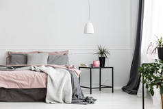 温暖的毯子和灰色枕头在一张舒适的双人床与肮脏的粉红色板料由白色卧室内部的空的墙壁
