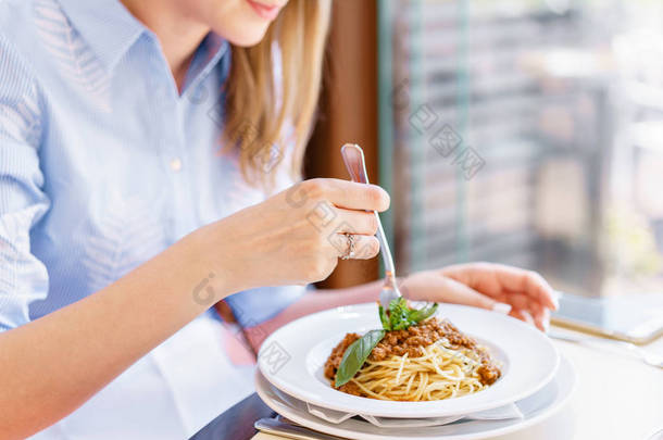 年轻快乐的女人坐在餐桌上的咖啡馆和享受的饭菜。饥饿的女人吃可口的面食。肉酱<strong>意大利</strong>面盘