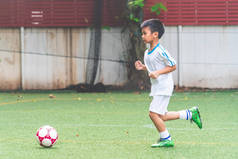 在学校足球比赛中，一个亚洲小男孩带着足球跑步 