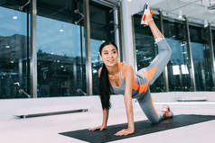 有吸引力的亚洲女孩微笑, 并在现代健身房的健身垫上做有氧运动