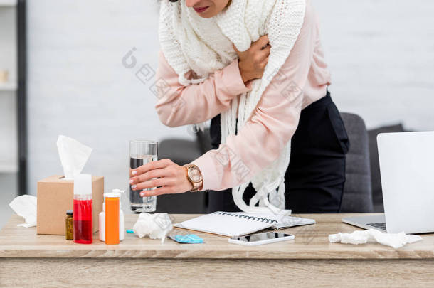 受折磨的年轻女实业家的短镜头从服务台拿着一杯水的药