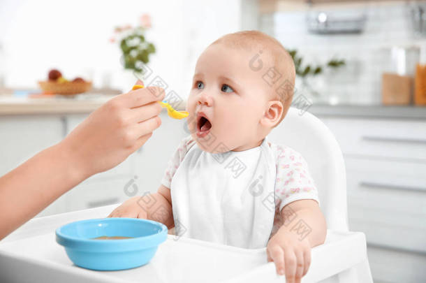 用勺子在厨房的母亲喂养的婴儿
