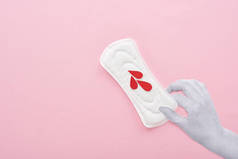 手拿着白色卫生巾，在粉红色背景上滴血的裁剪视图