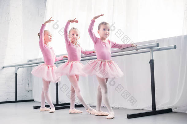 在芭蕾舞室跳舞的粉红色短裙裙的可爱的小孩子的全长视图 