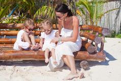 年轻妈妈，有可爱的女儿，坐在沙滩椅和享受他们的假期