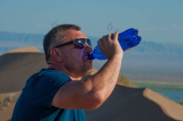 一<strong>个人</strong>在沙漠山顶的沙丘上喝水。 口渴