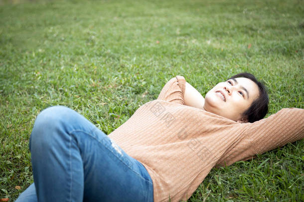 快乐的亚洲<strong>女人</strong>躺在公园的草地上休息时感到很舒服，<strong>女人</strong>手挽着头，享受<strong>呼吸</strong>新鲜空气，周末做完家务活后在绿色的自然中放松