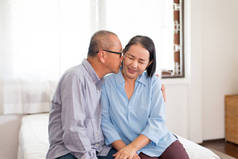 在家里，一对快乐的老亚洲情侣在床上亲吻着脸蛋