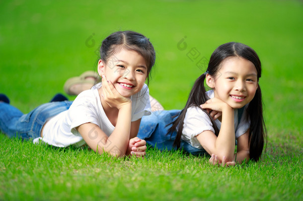 躺在<strong>绿草</strong>地上的两个小的亚洲女孩