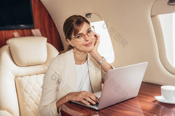 漂亮的女商人，穿着手提电脑，看着私人飞机上的相机 