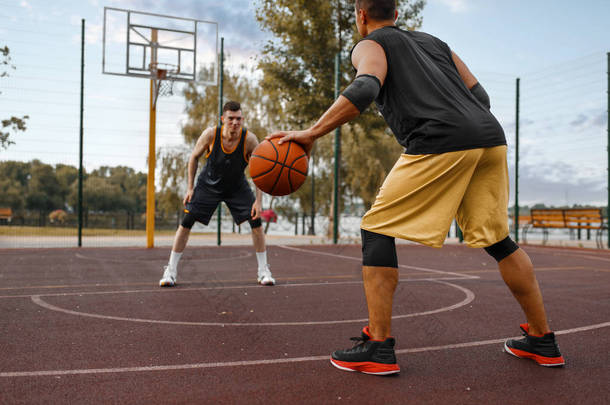 两名篮球运动员在室外场地上练习战术. 男子运动员穿着运动服在街头篮球训练中比赛