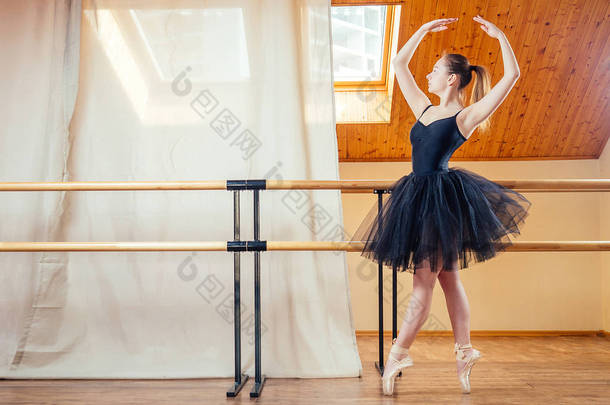 穿着芭蕾舞裙跳舞的年轻貌美的女人。 芭蕾舞演员在教室里热身. 那个穿着漂亮黑色连衣裙的芭蕾舞女.