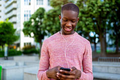 微笑的年轻黑人男子听音乐与Mp3播放器手机的肖像