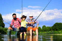 小男孩和他的父亲和祖父一起在湖上钓鱼。夏天的一天快乐的祖父，父亲和孙子，带着钓竿在河里。快乐的人一家人一起钓鱼，一起玩乐.