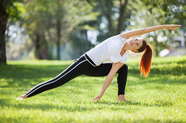 瑜伽在室外。快乐的女人做瑜伽练习，伸展在公园里。大自然<strong>中</strong>的瑜珈冥想。健康的生活方式和放松的概念。漂亮的女人在<strong>草</strong>地上练习瑜伽