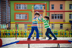 两个小学校和学龄前男孩一起在户外操场上玩耍。在阳光明媚的夏日，孩子们站在户外活动的圆木上竞争