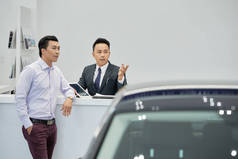 年轻的越南汽车经销店工人向富有的顾客展示汽车
